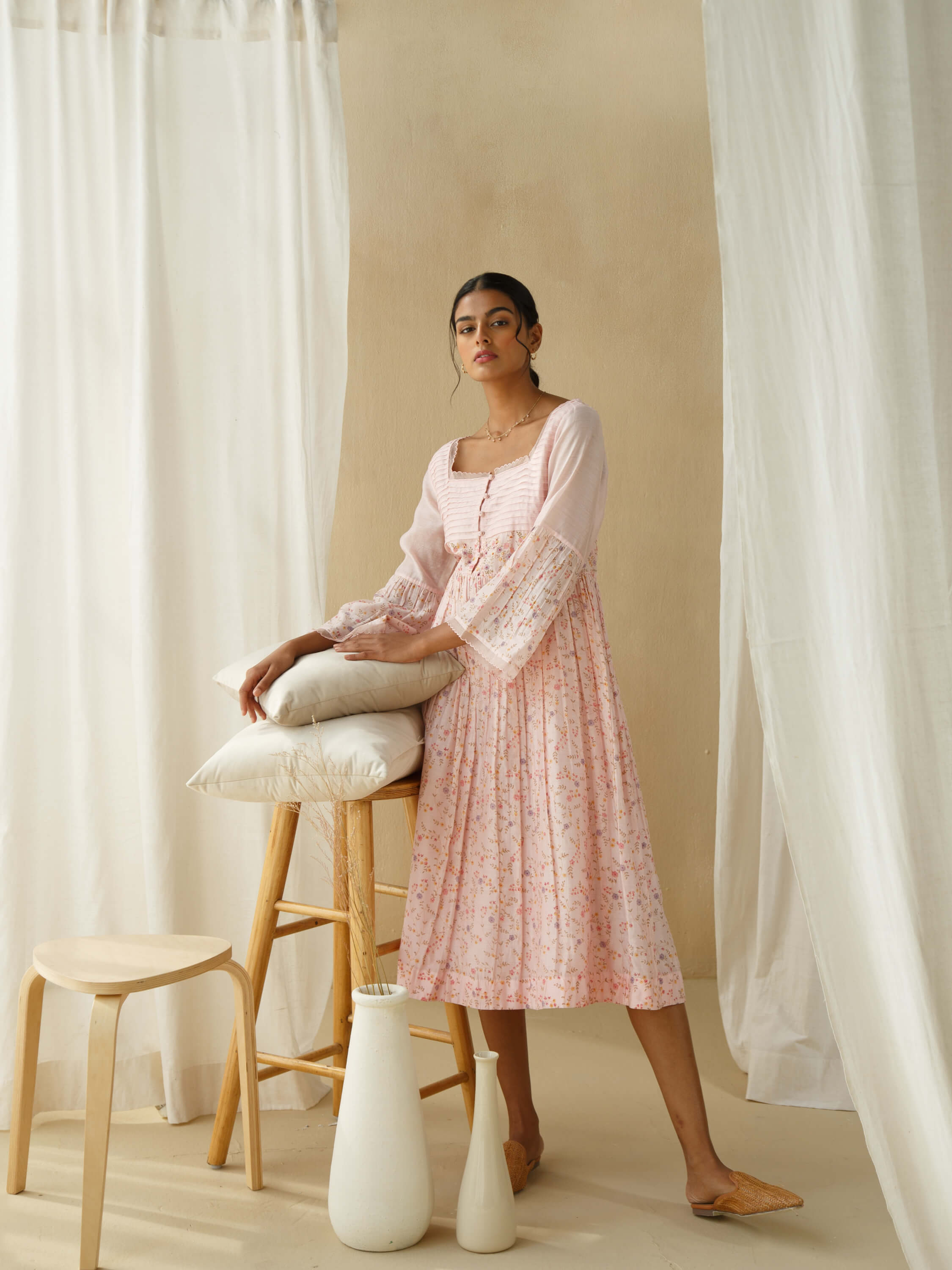 Elegant woman in pink floral dress leaning on stool, minimalist decor