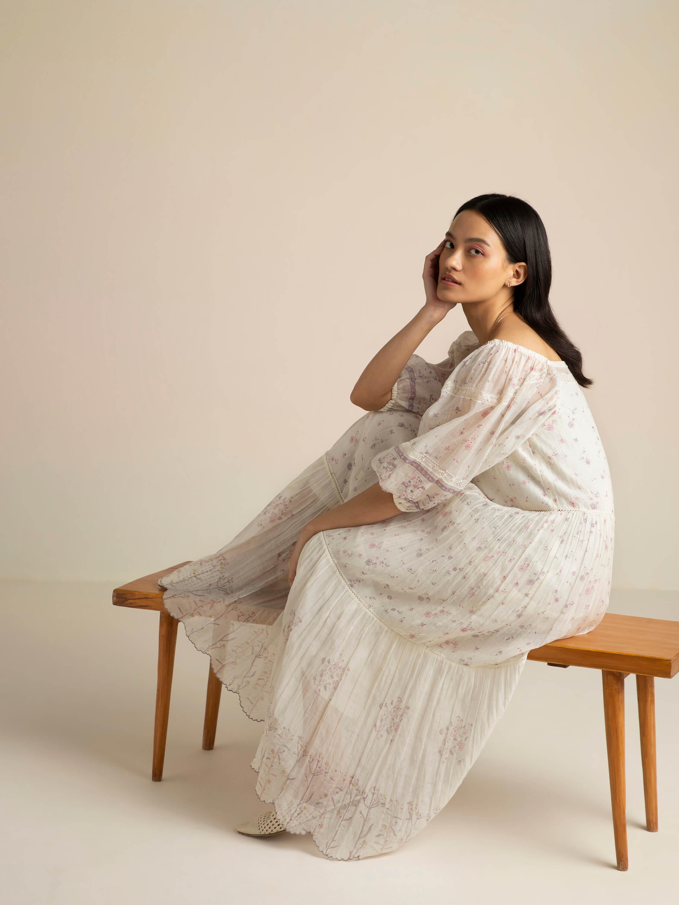 Woman in floral dress seated thoughtfully on a wooden bench.