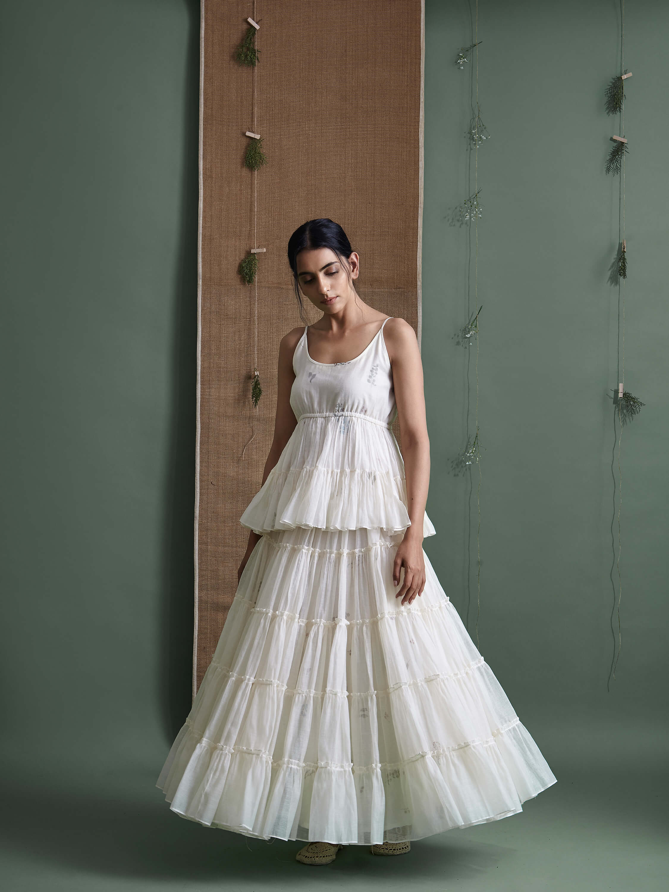 Woman in a white tiered dress standing against green wall.