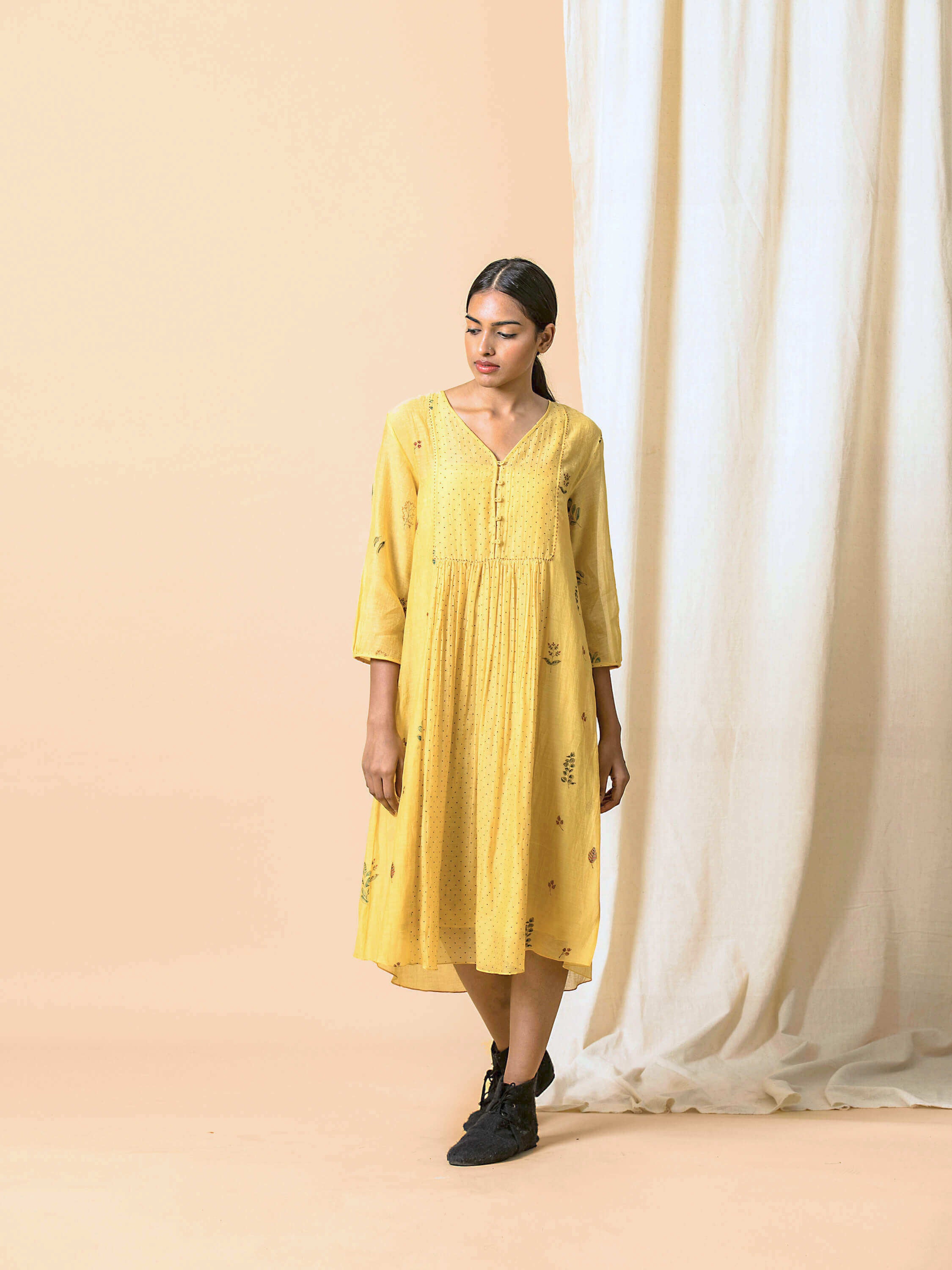 Woman wearing yellow midi dress with floral patterns in minimalist setting