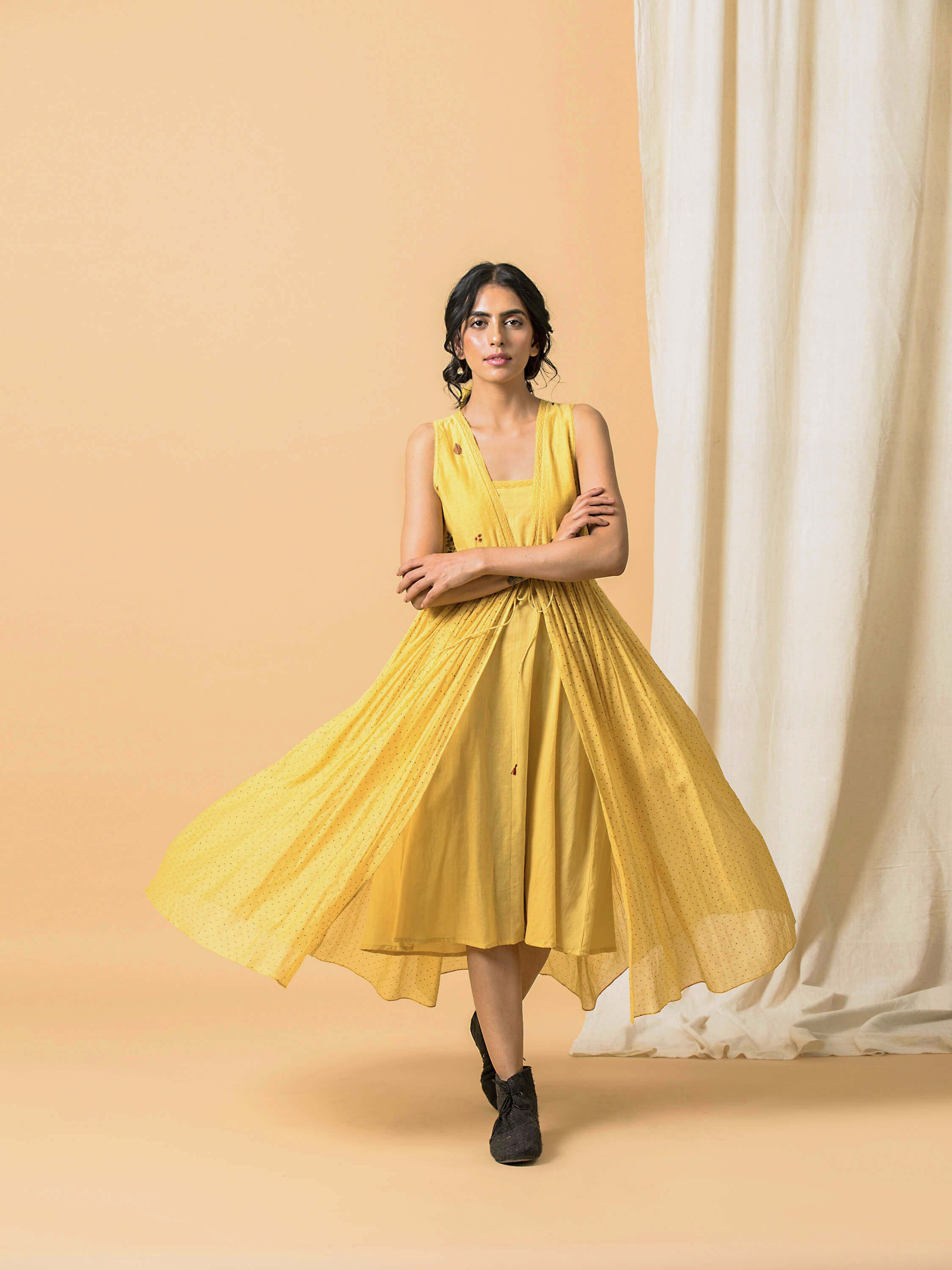 Woman in a flowing yellow dress posing against a beige background.