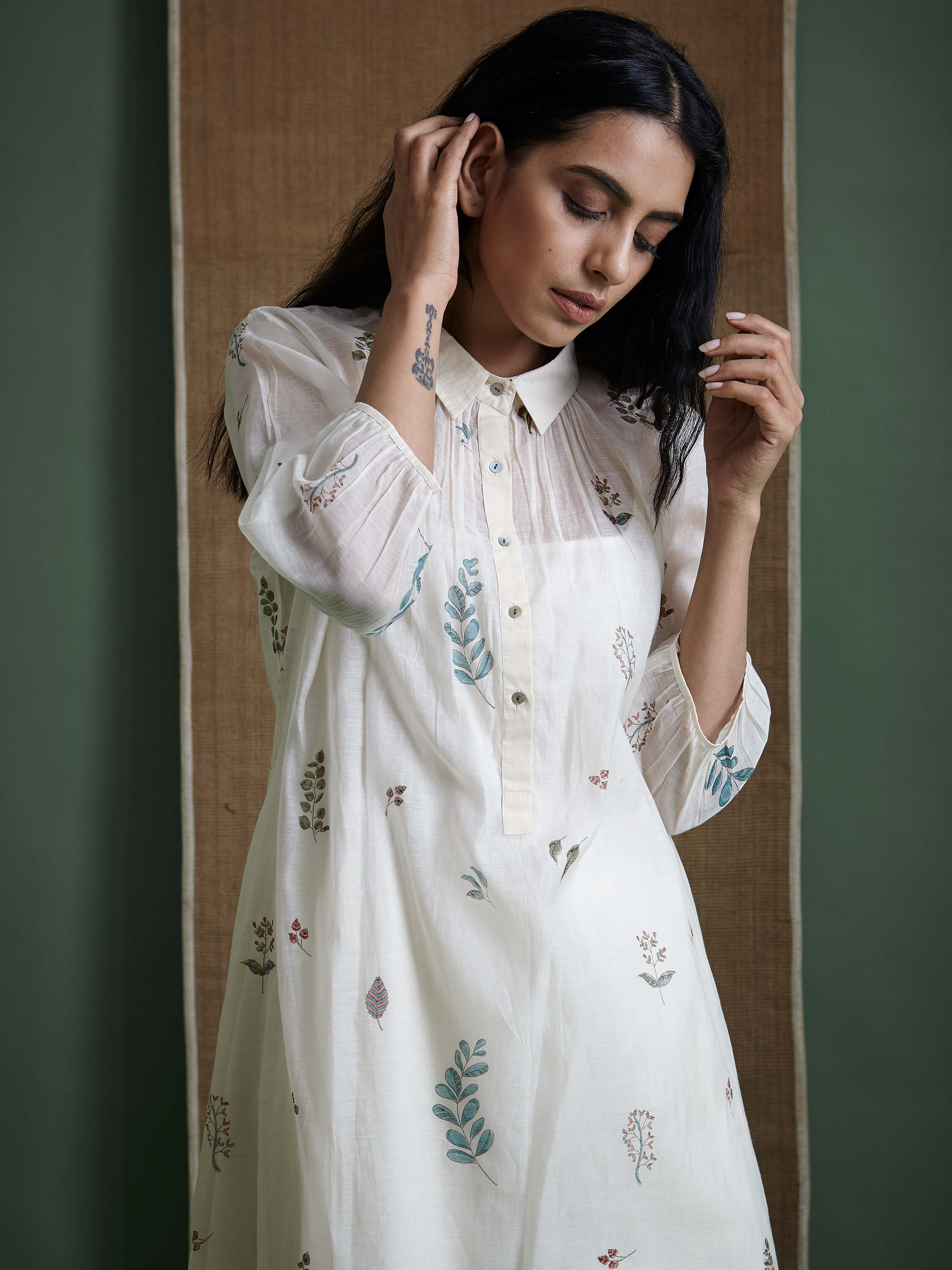 Woman wearing embroidered white dress posing against neutral background.