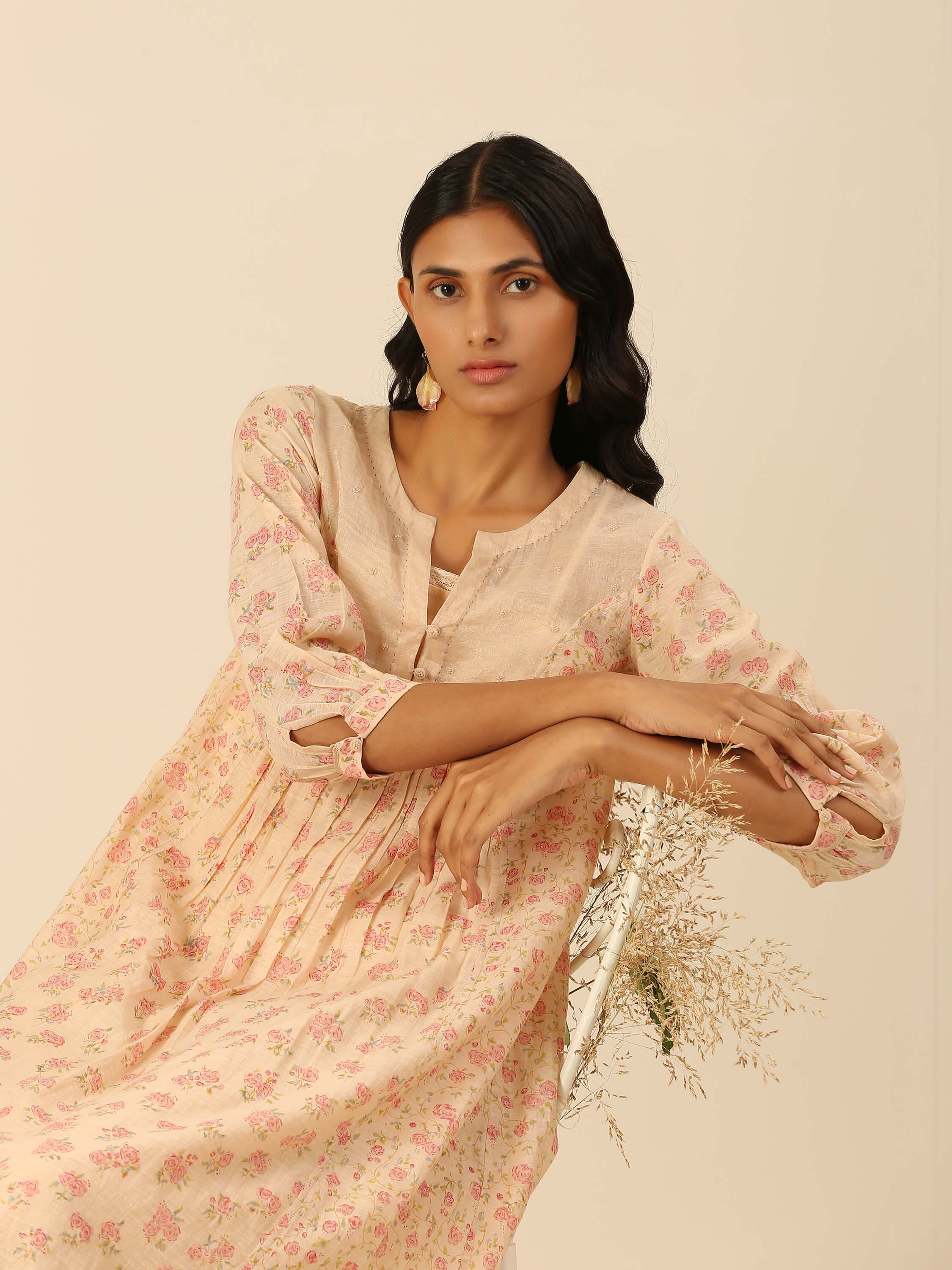 Woman in floral beige dress posing with dried flowers.