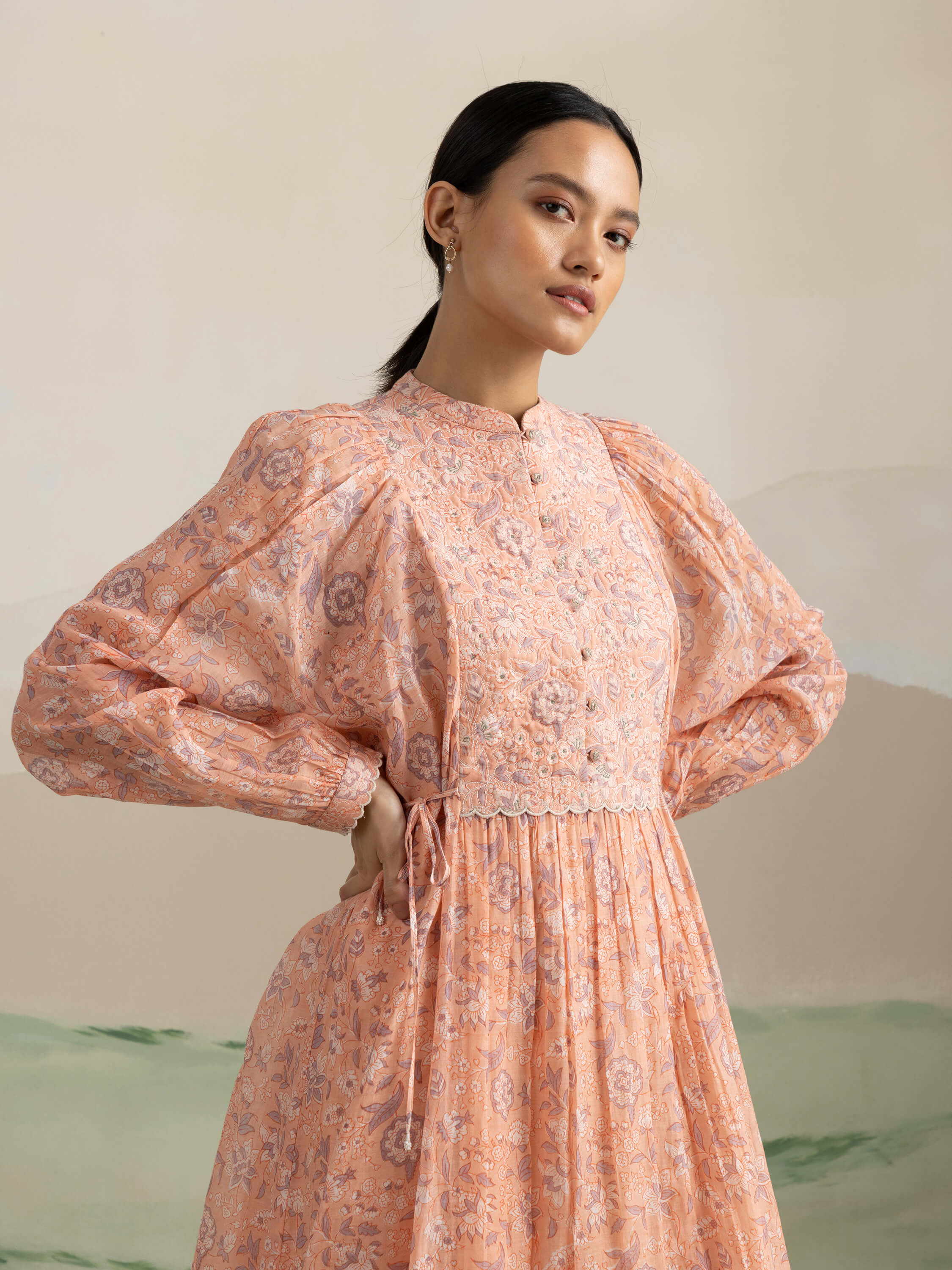 Woman wearing a floral peach long-sleeve dress with intricate details.