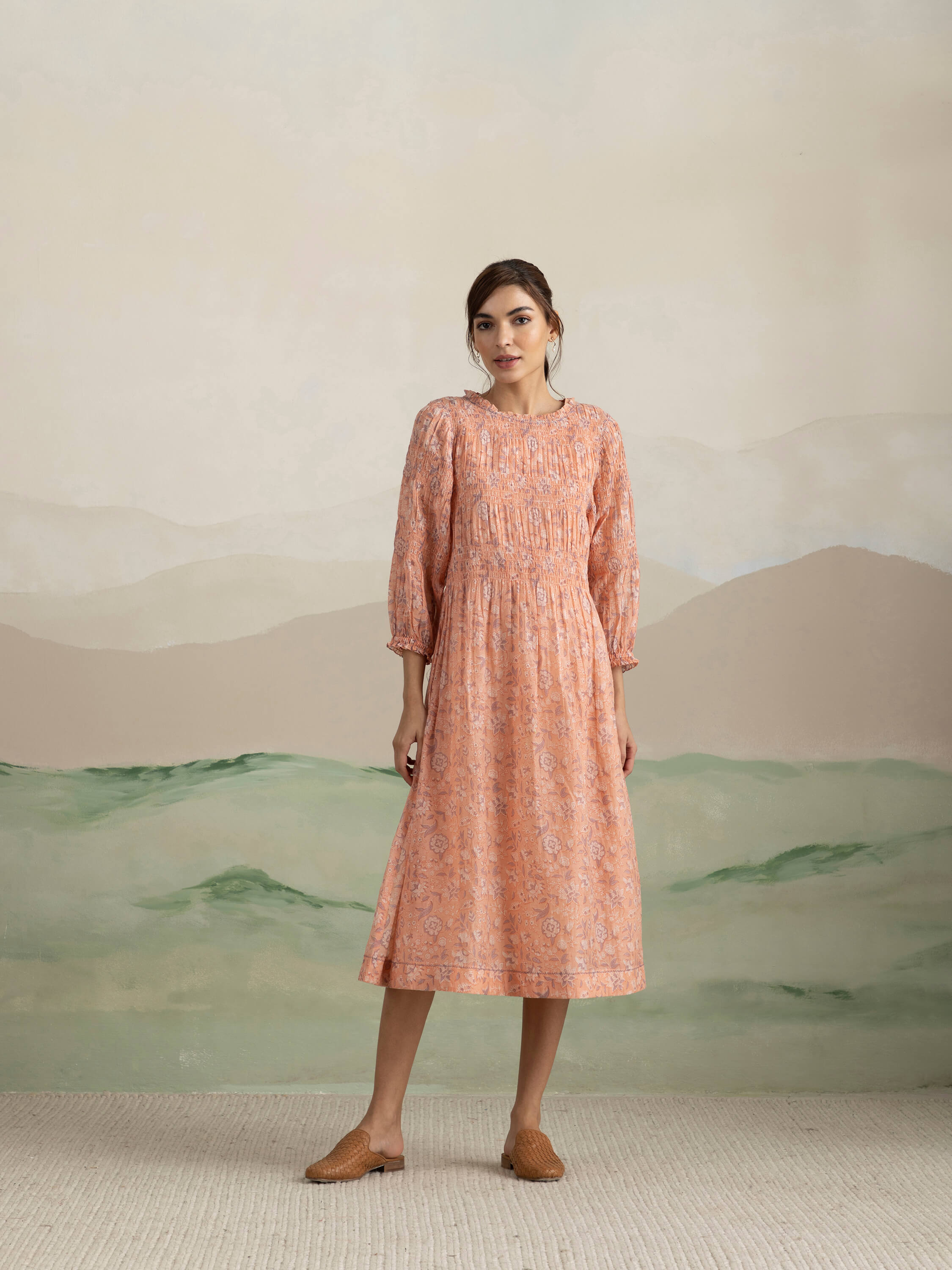 Woman in peach floral dress standing against scenic backdrop.