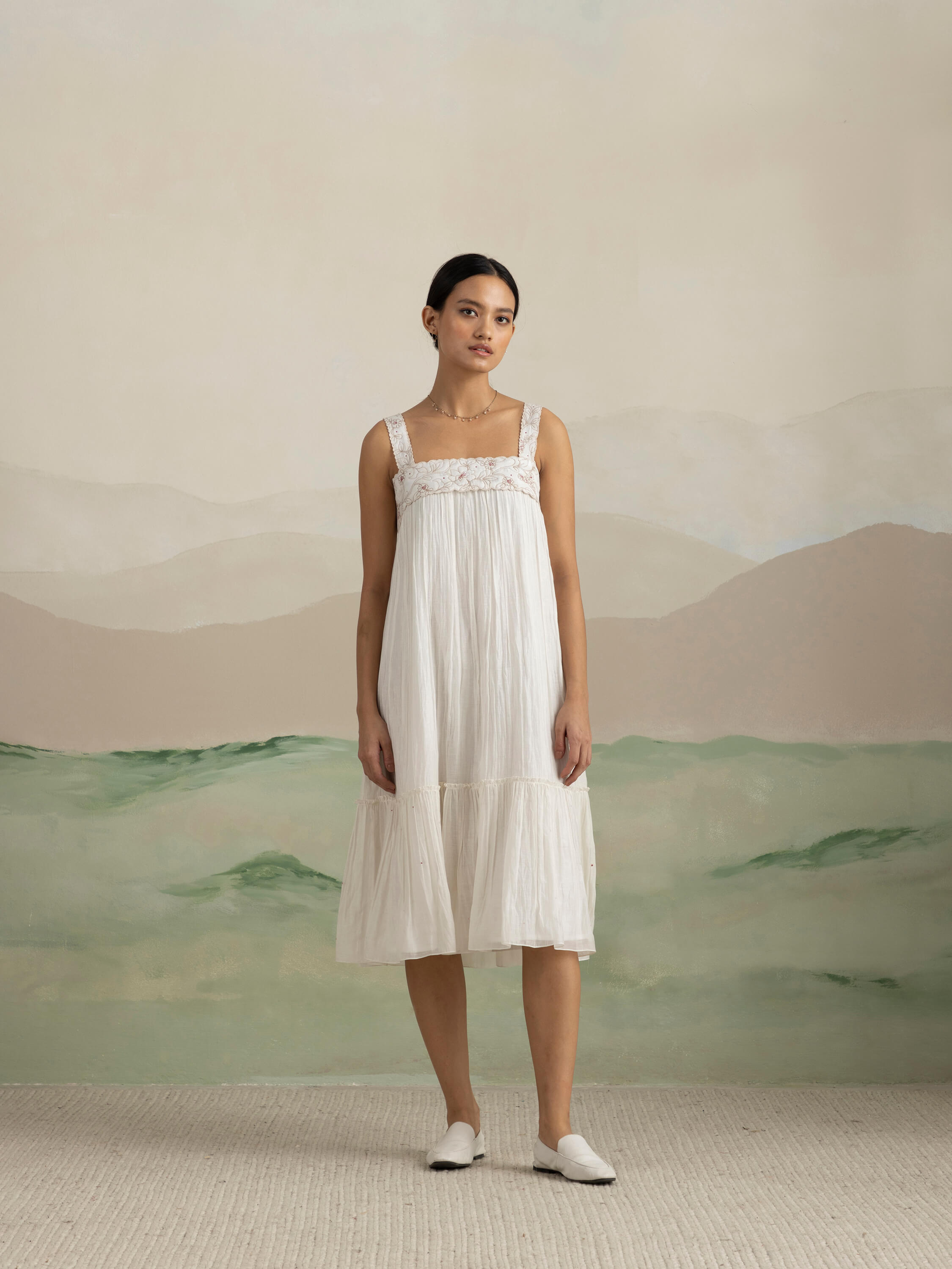 Woman in white summer dress standing in front of a neutral backdrop.