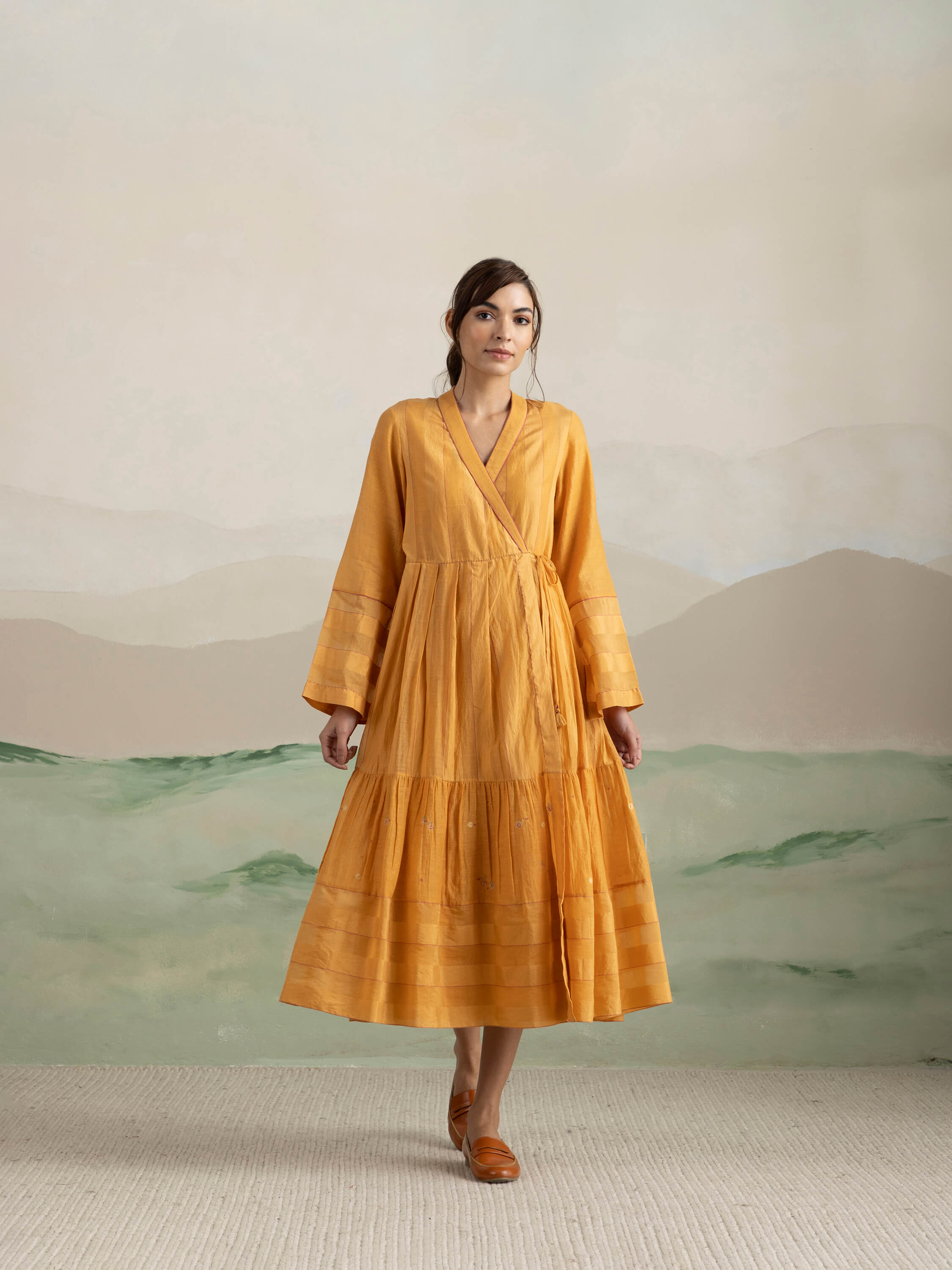 Woman in mustard yellow dress against a pastel background.