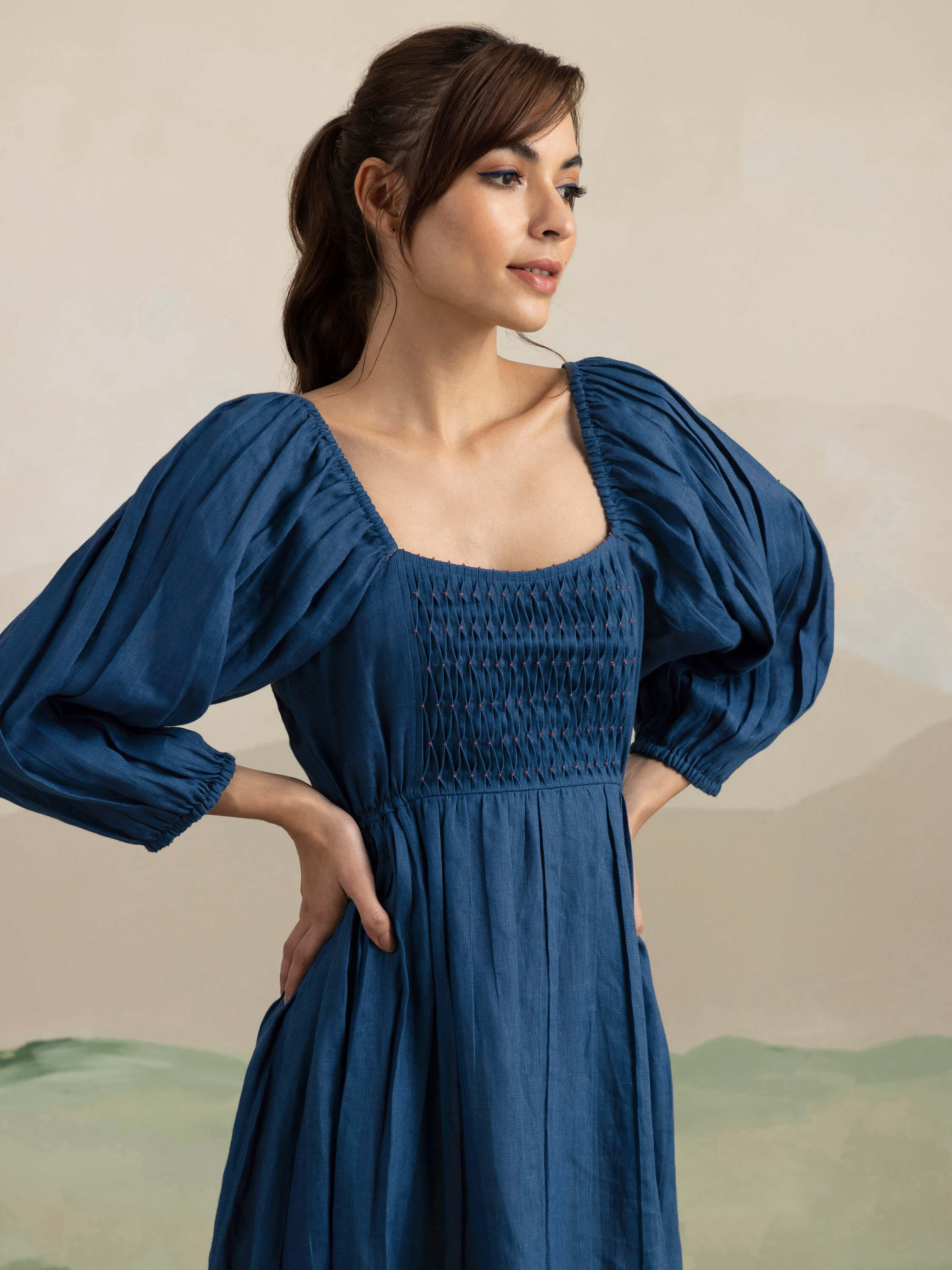 Woman in blue long-sleeved dress posing against neutral background.