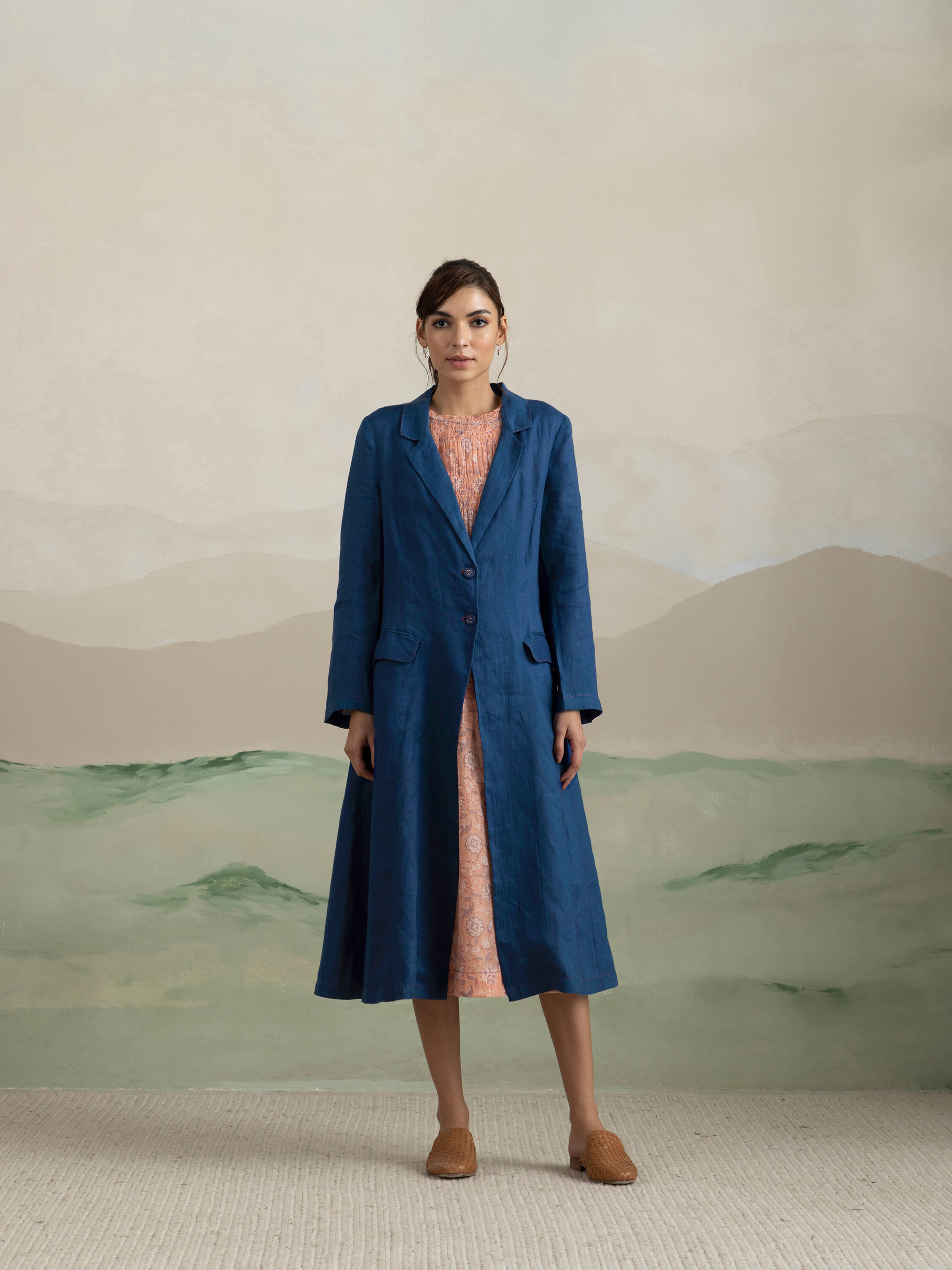 Woman in a blue coat and pink dress, minimalist background.