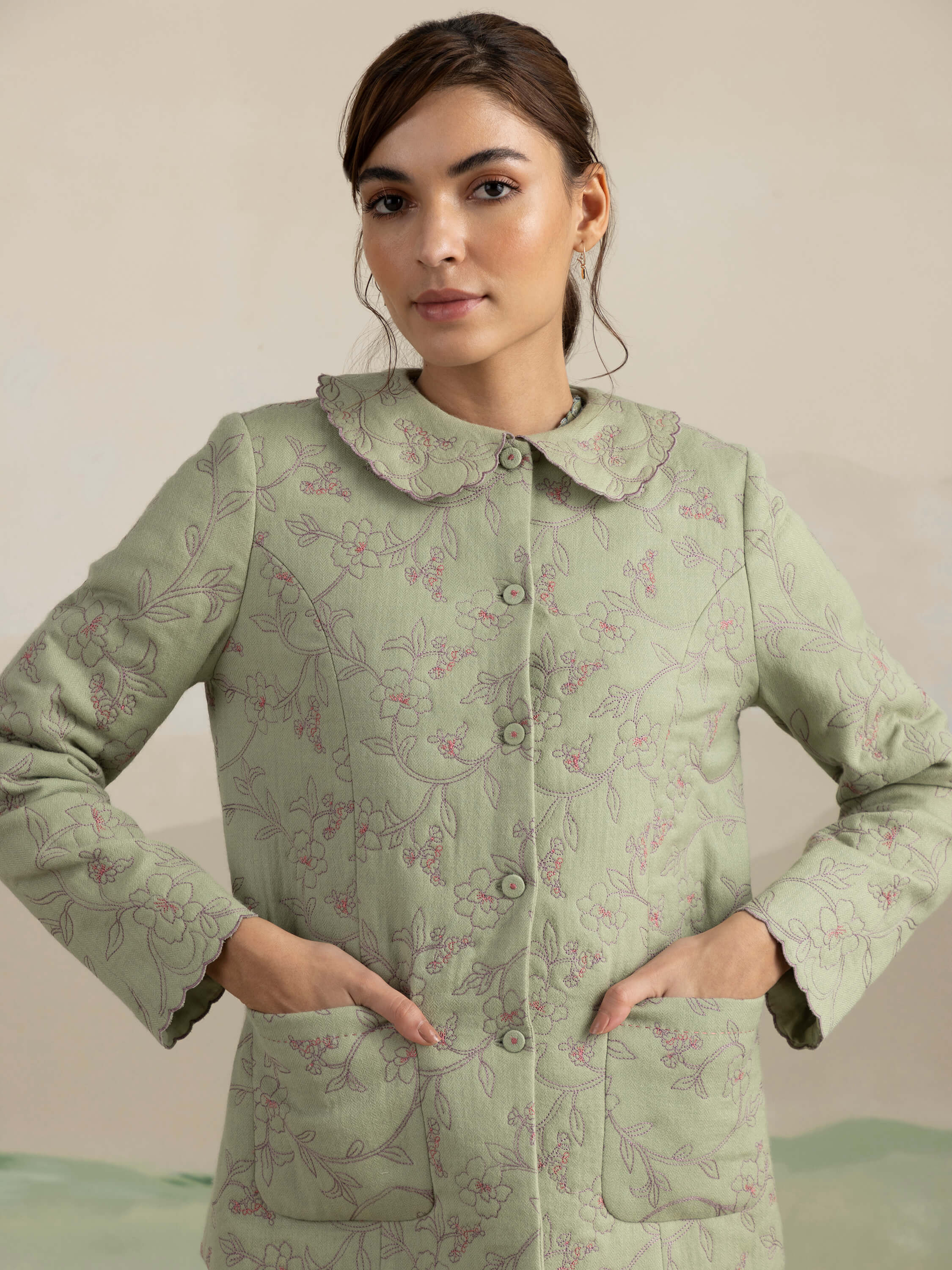 Woman wearing a green floral embroidered jacket with pockets.