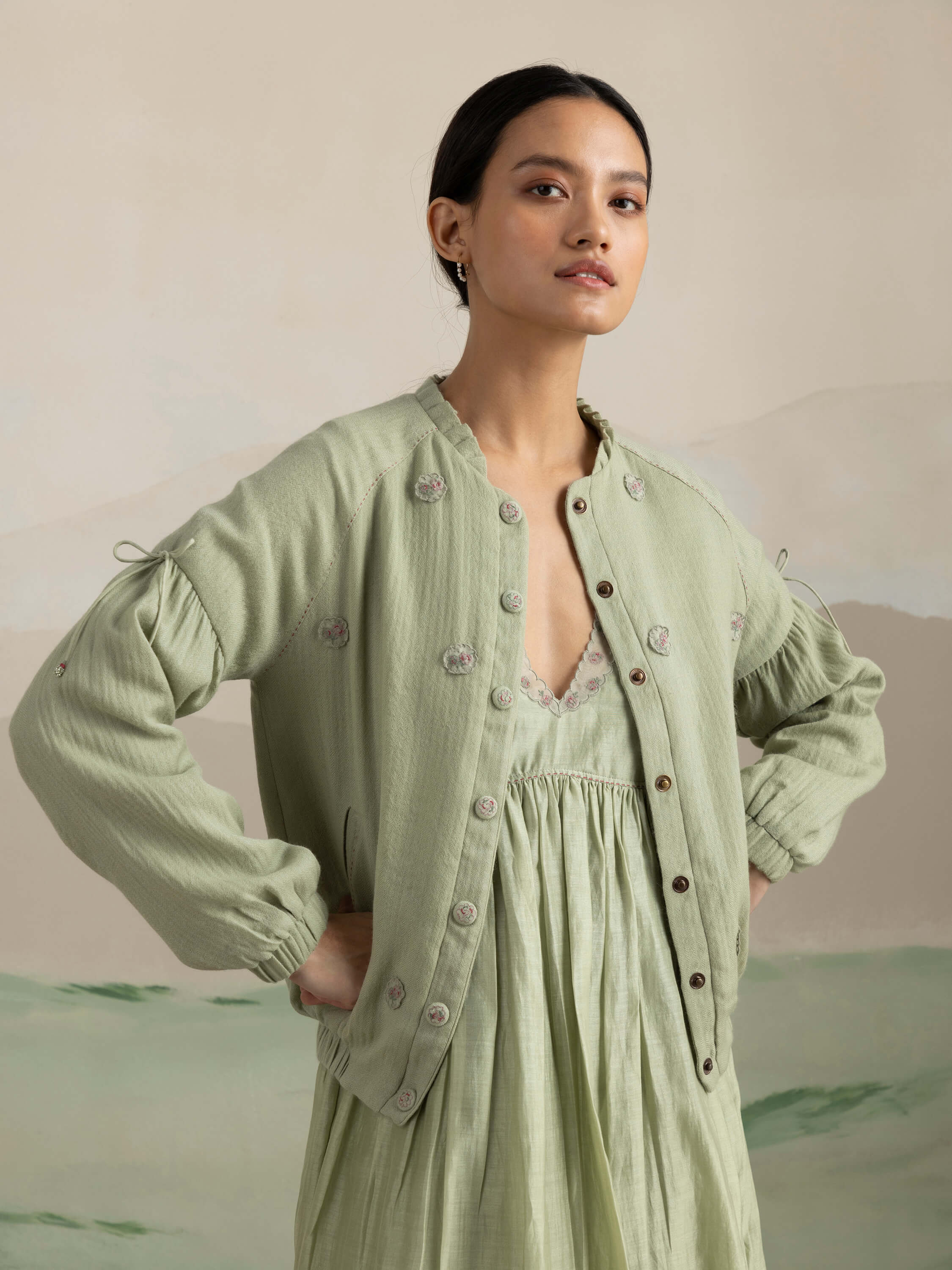 Woman modeling green button-up jacket and dress combo in minimalist setting.