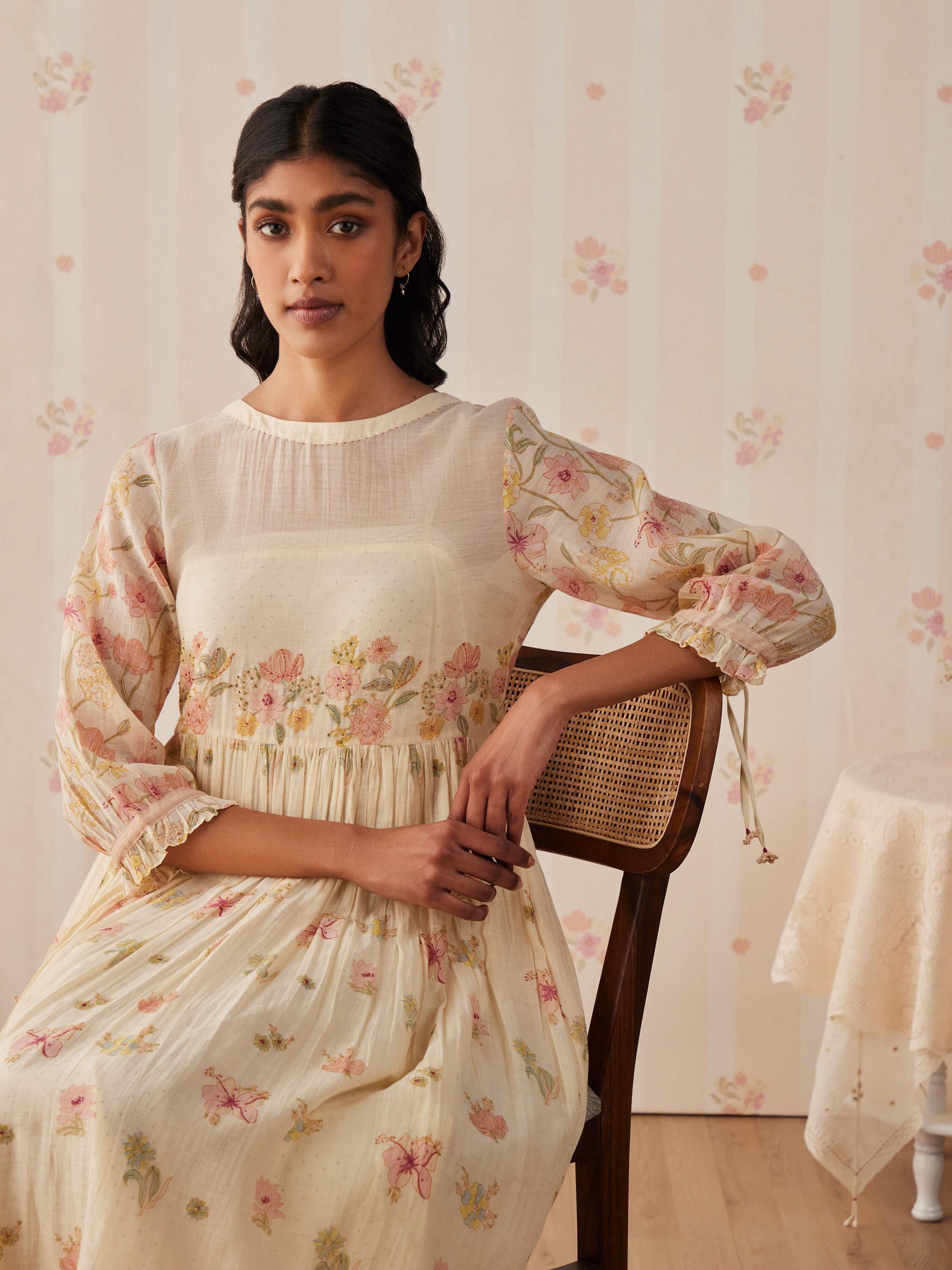 Woman in floral dress sitting on a chair indoors.