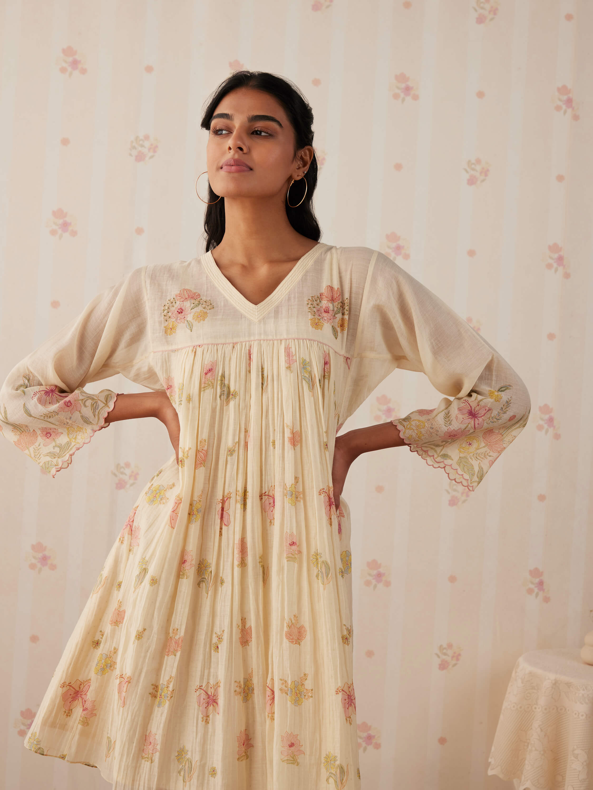 Woman modeling cream floral embroidered dress with flared sleeves.