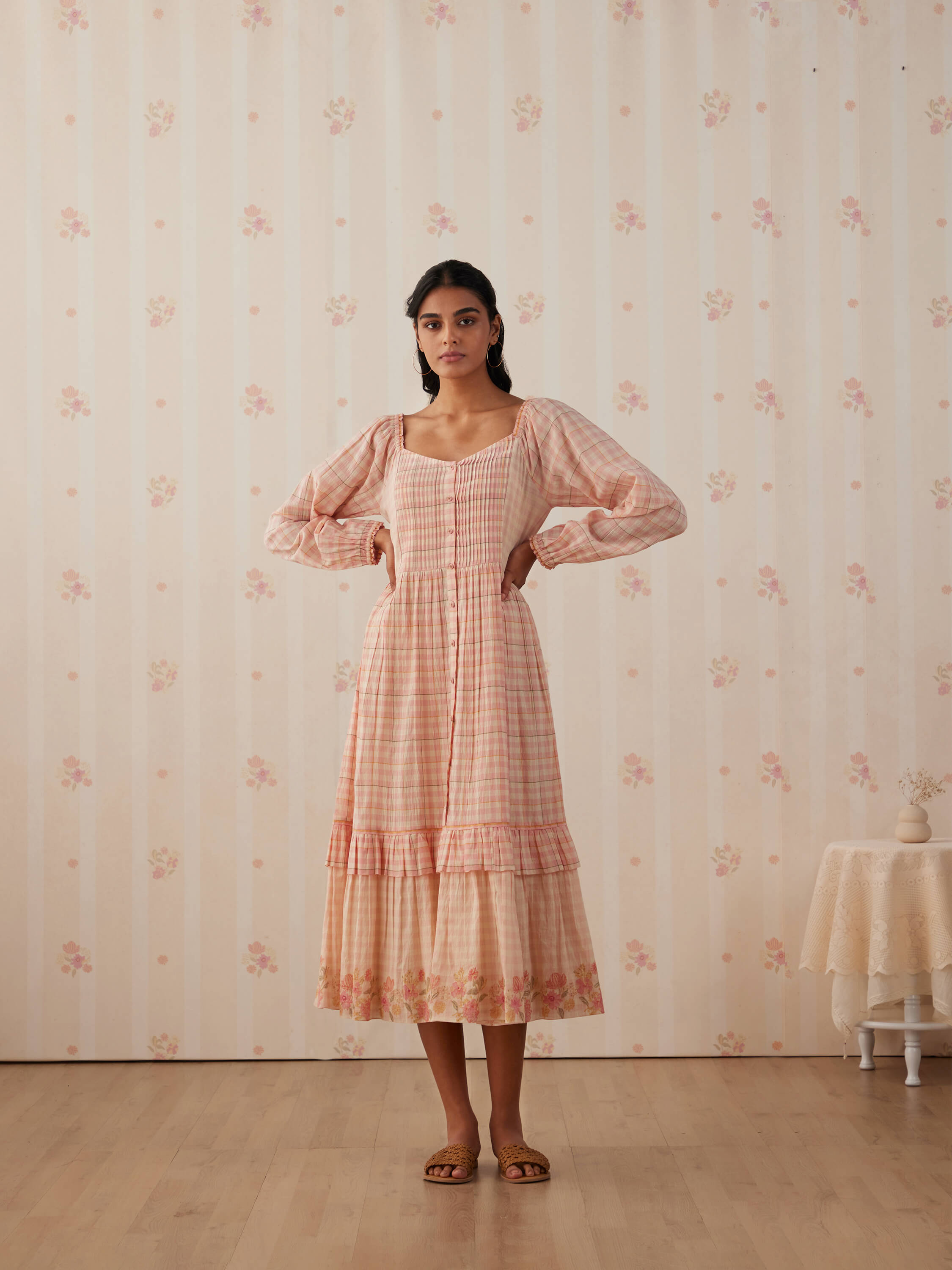 Woman in pink checked dress in floral-themed room.