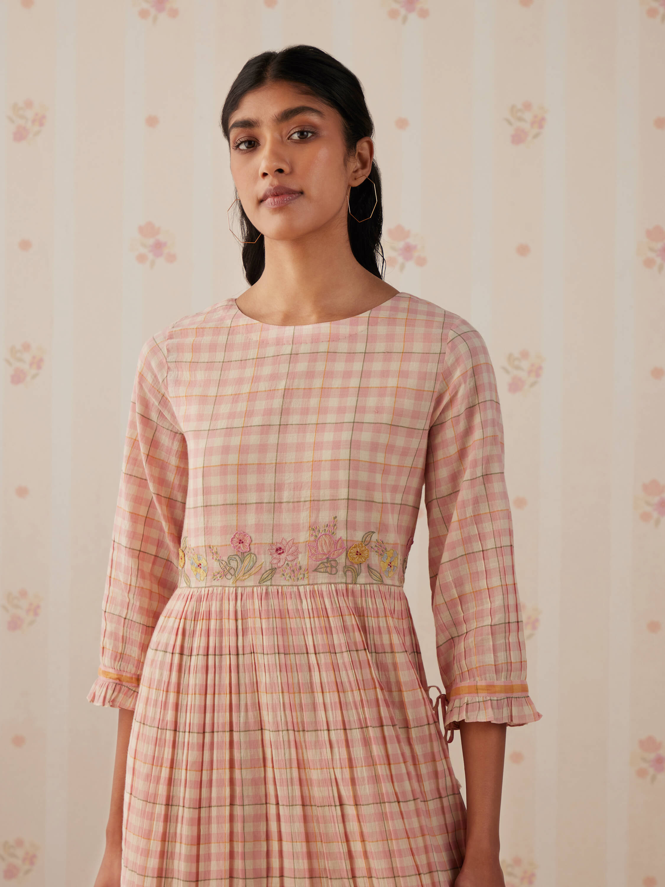 Woman in pastel plaid dress with floral embroidery on waist.