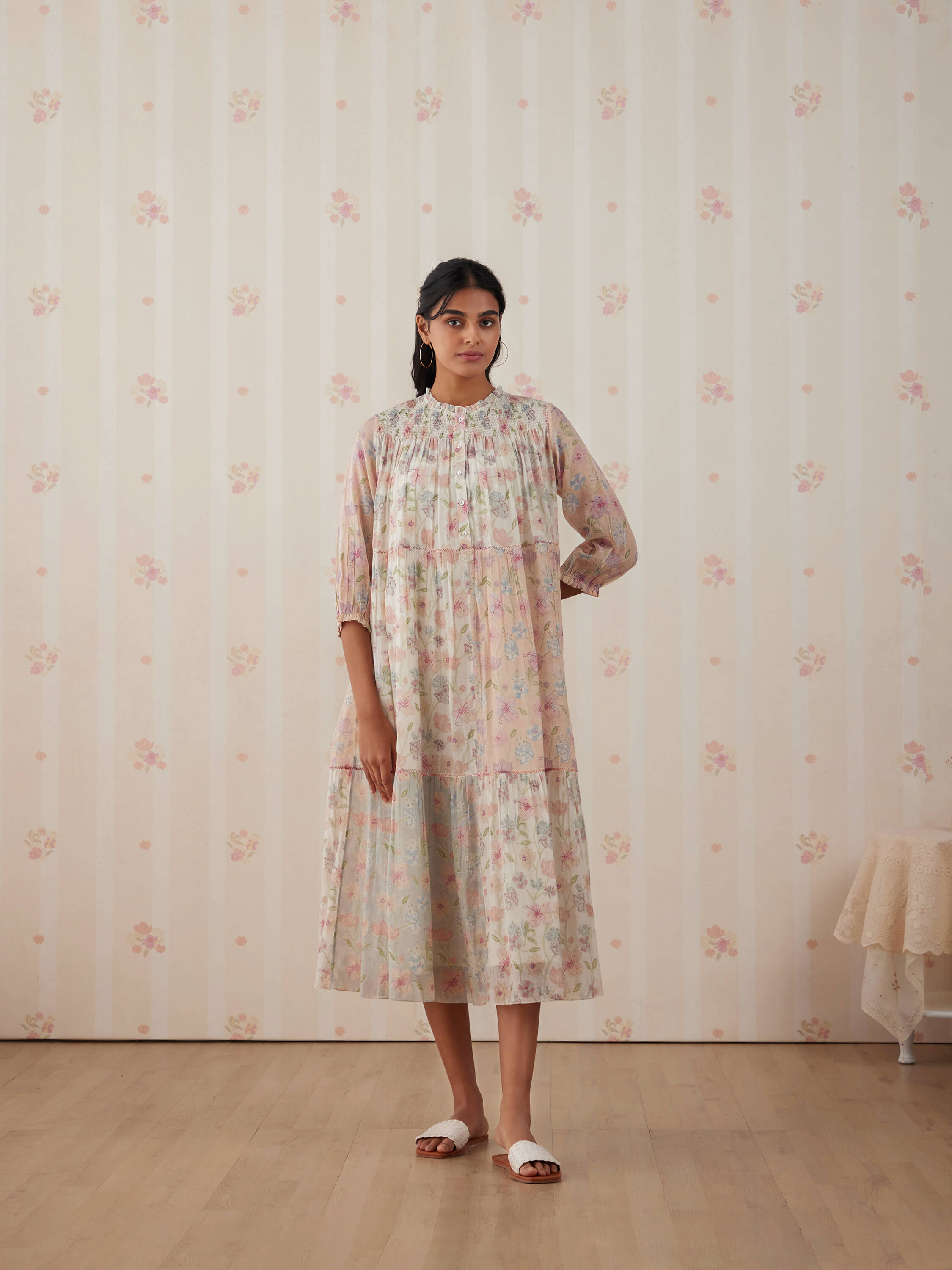 Woman in floral dress standing against pastel floral wallpaper.