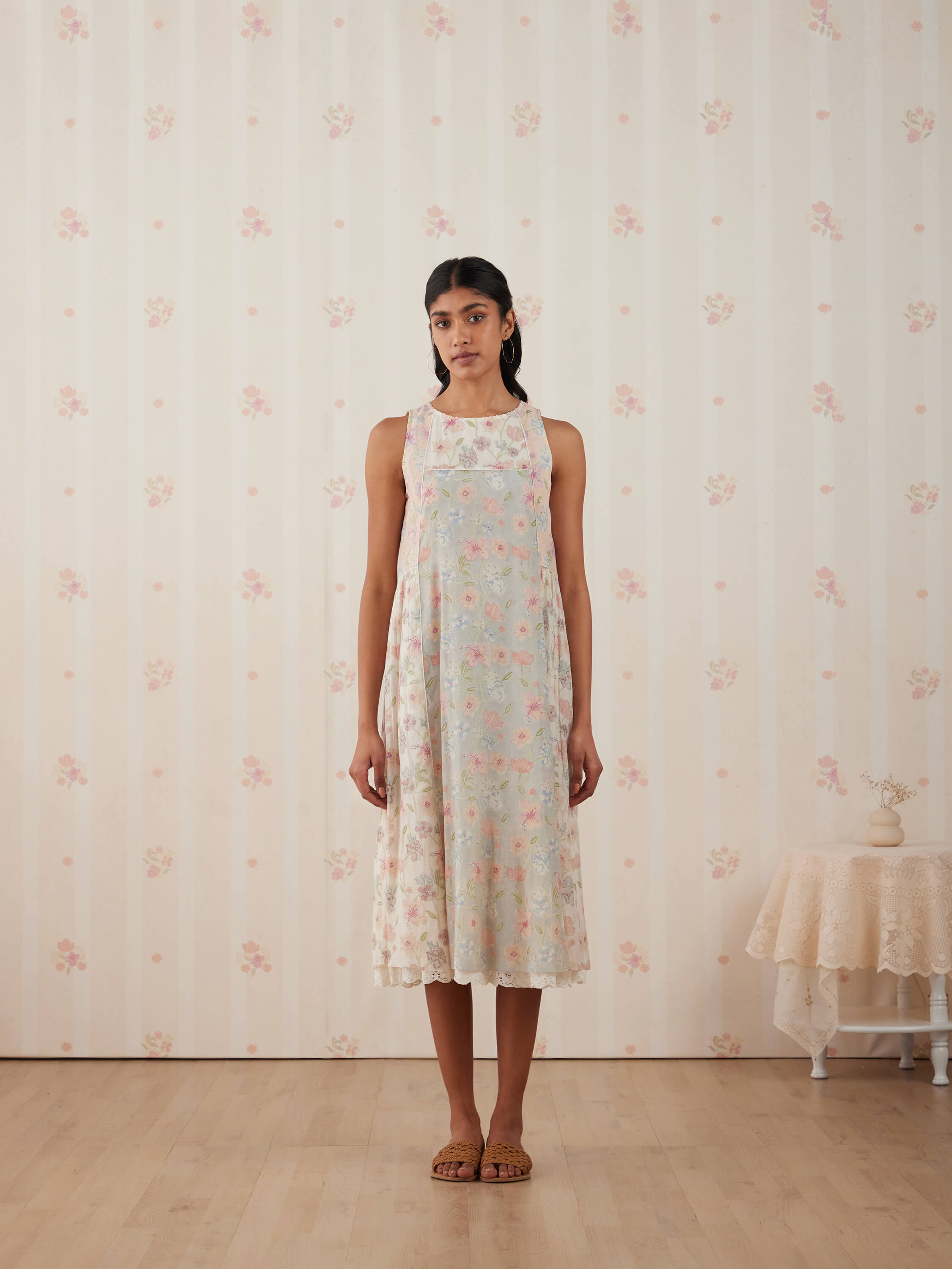 Woman wearing floral dress standing against vintage wallpaper background.