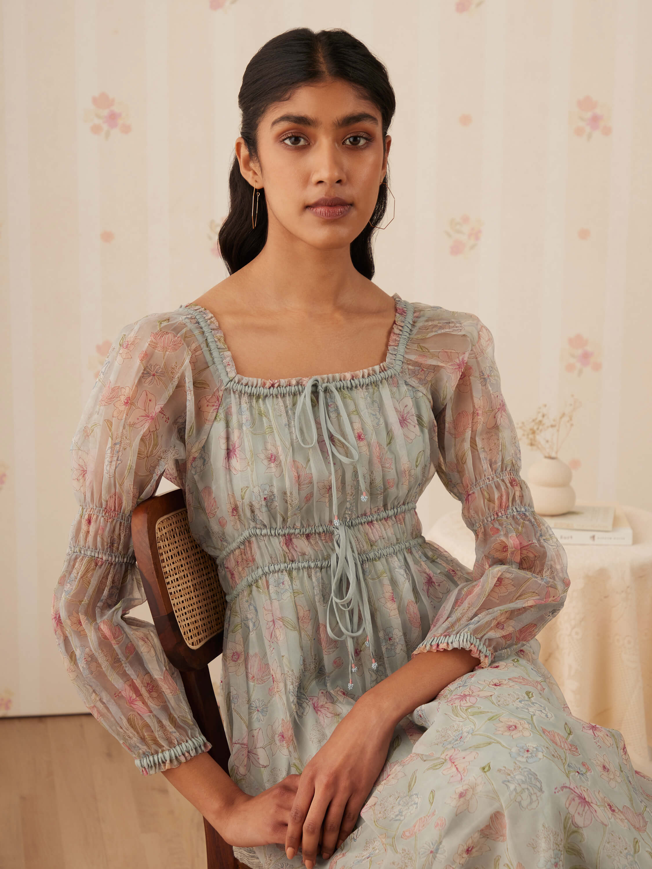 Woman in floral embroidered dress sitting on chair indoors.